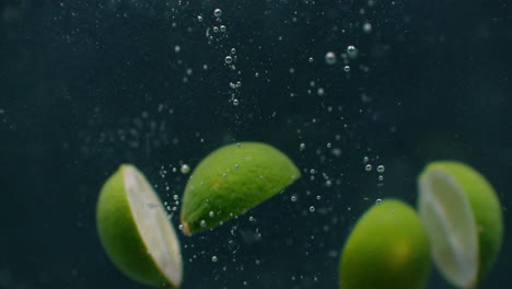 Green-limes-are-thrown-into-a-container-of-water.-Video-of-fruit-in-slow-motion